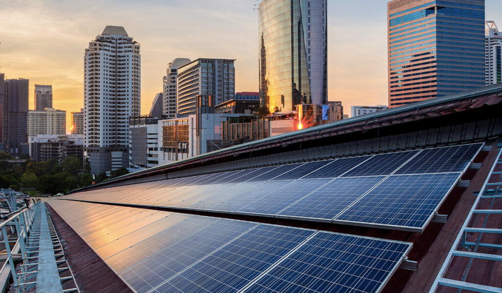 Solar panels installed on a rooftop in front of modern city buildings at sunset, representing clean energy in an urban setting